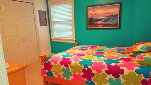 Un dormitorio con una colcha estampada de flores coloridas, un cuadro de un atardecer y una pared color turquesa.