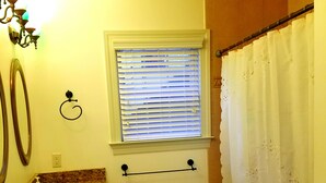 Un baño con dos lavamanos, una ventana con persianas, un perchero para toallas, una cortina de ducha y un tapete estampado.