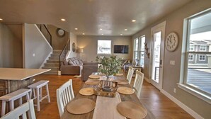 Un salón amplio con comedor, una escalera y ventanas grandes.