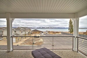 Een balkon met uitzicht op een parkeerplaats en gebouwen, een bankje en een bergketen op de achtergrond.