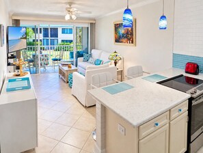 A modern kitchen with a central island, a dining area with a sofa and chairs, and a view of a balcony with outdoor furniture.