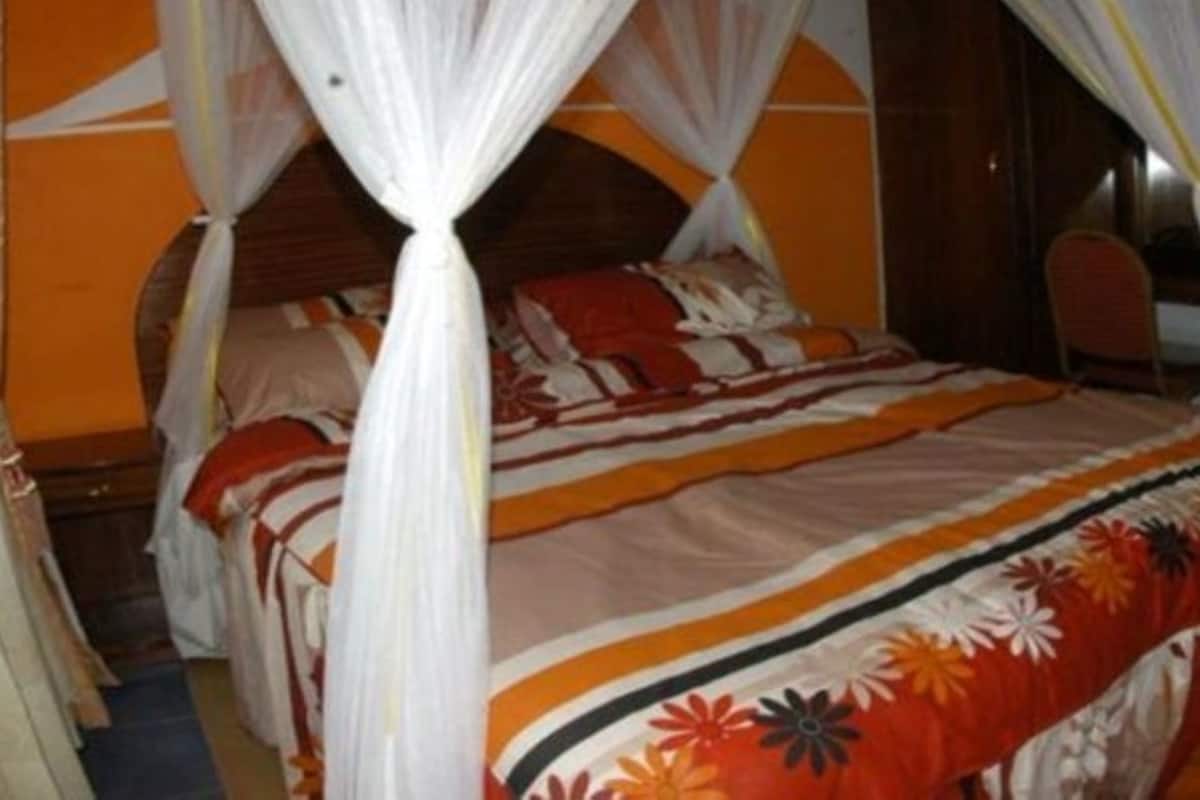 Una cama con dosel, una silla y un escritorio en una habitación con paredes anaranjadas.