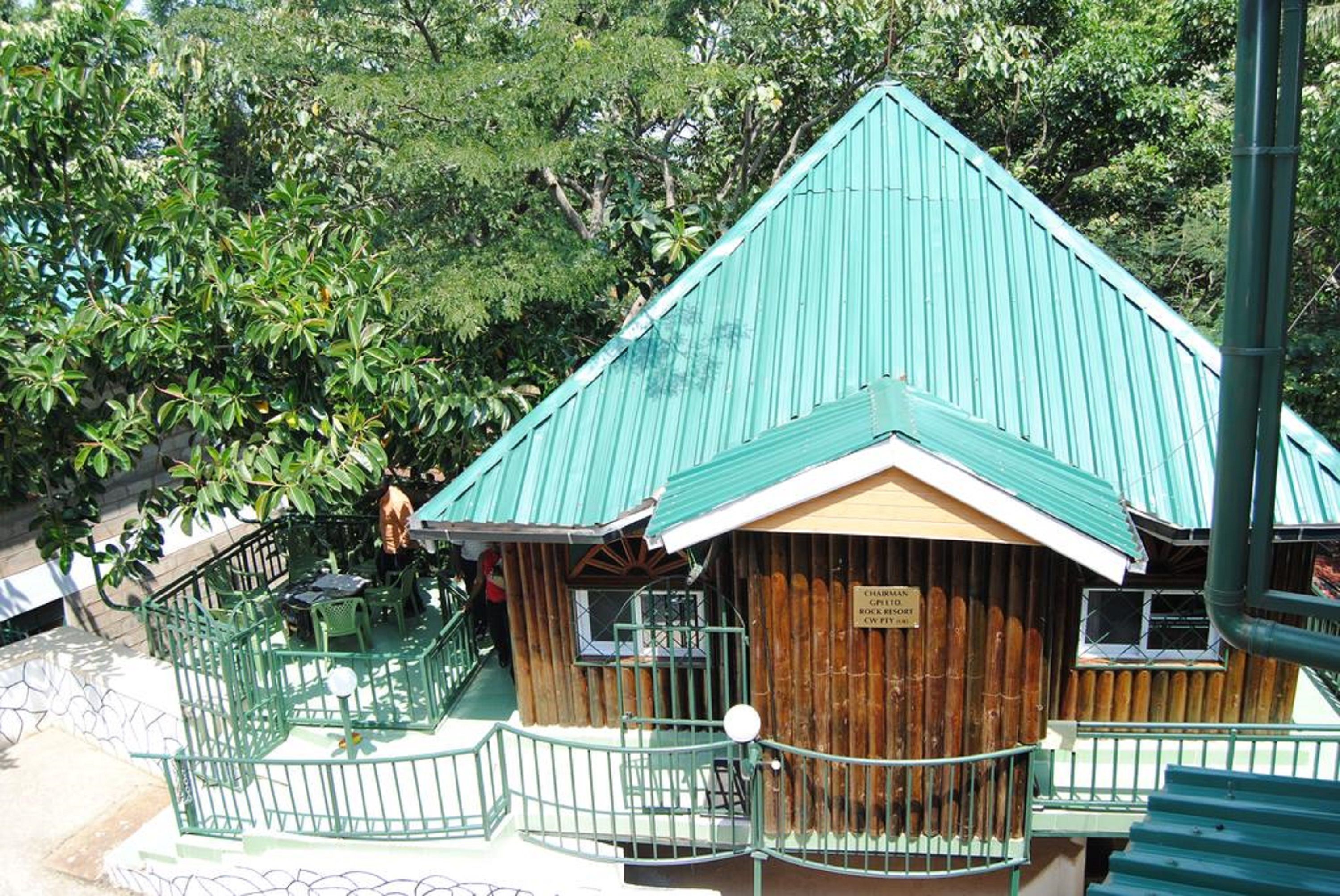 A wooden building with a green roof, surrounded by greenery.