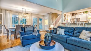A spacious living room with a blue sofa, a coffee table with a vase, and a dining area with a white table and chairs.
