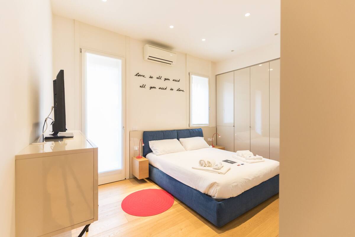 Un dormitorio moderno con cama, mesitas de noche, televisor y armario.