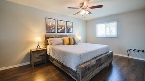 A bedroom with a bed, wooden headboard, nightstands, a ceiling fan, and framed artwork on the wall.