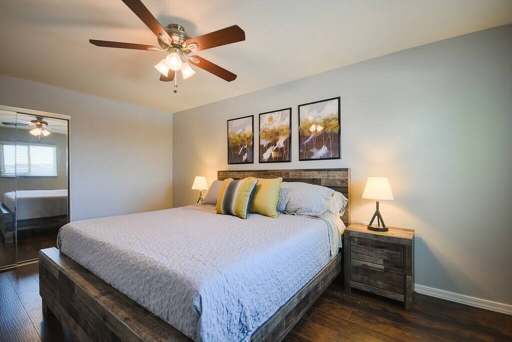 Een slaapkamer met een groot bed, een plafondventilator, bedlampen en een wanddecoratie.