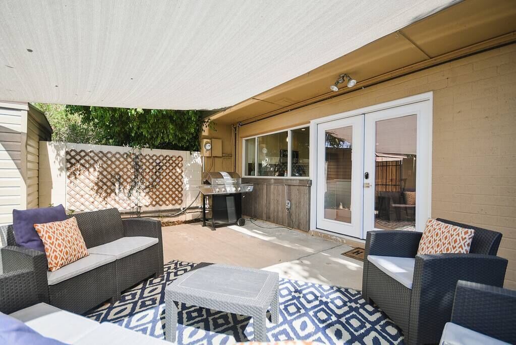 Un espace extérieur aménagé en terrasse, avec des meubles en osier, un barbecue et un tapis à motifs.