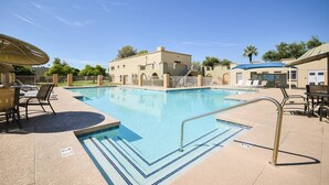 A swimming pool with lounge chairs and a covered area, surrounded by buildings and trees.