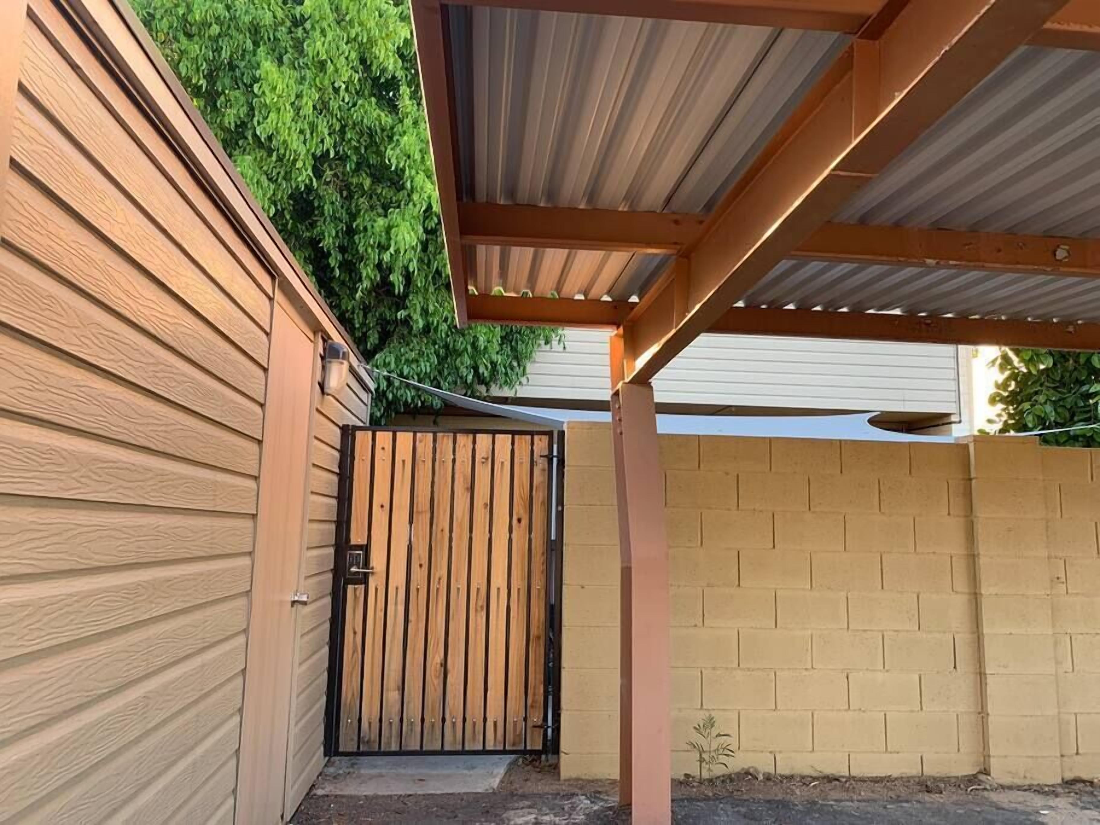 Un espace extérieur abrité, doté d’un portail en bois, d’un mur en briques et d’une structure de toit en métal.