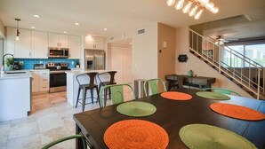A modern kitchen with white cabinets, a stainless steel refrigerator, and a microwave. There is a dining area with a dark wooden table and colorful placemats.