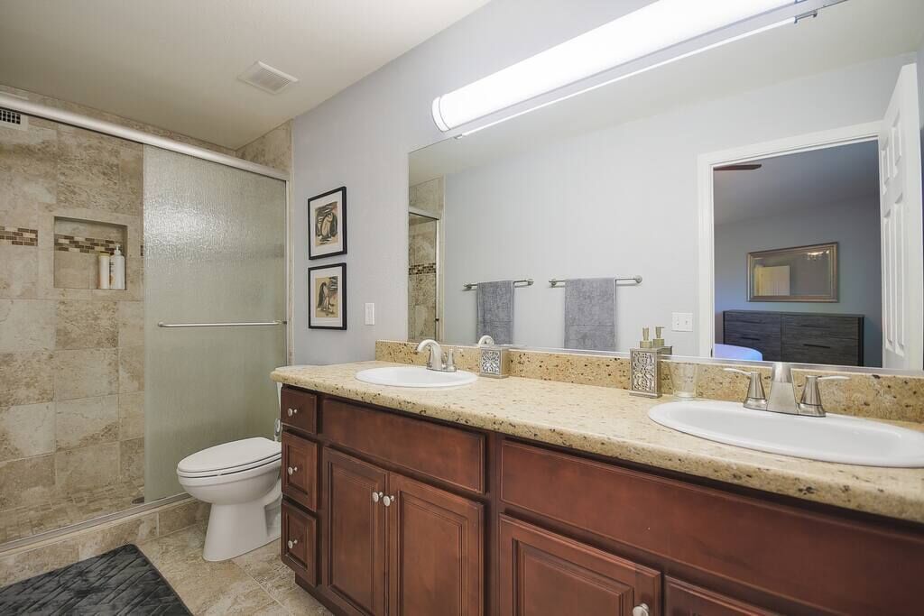A bathroom with two sinks, a toilet, a shower, and a large mirror.