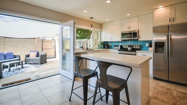 A modern kitchen with a central island, stainless steel appliances, and a sliding glass door leading to a patio area with outdoor seating.