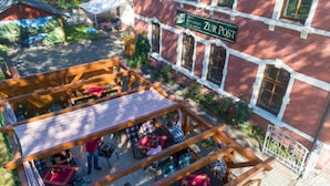 An outdoor seating area with tables and chairs, a wooden pergola, and a view of a red brick building with a sign reading "Hotel Restaurant Biergarten ZUR POST". - Landhotel zur Post (Schoenheide)