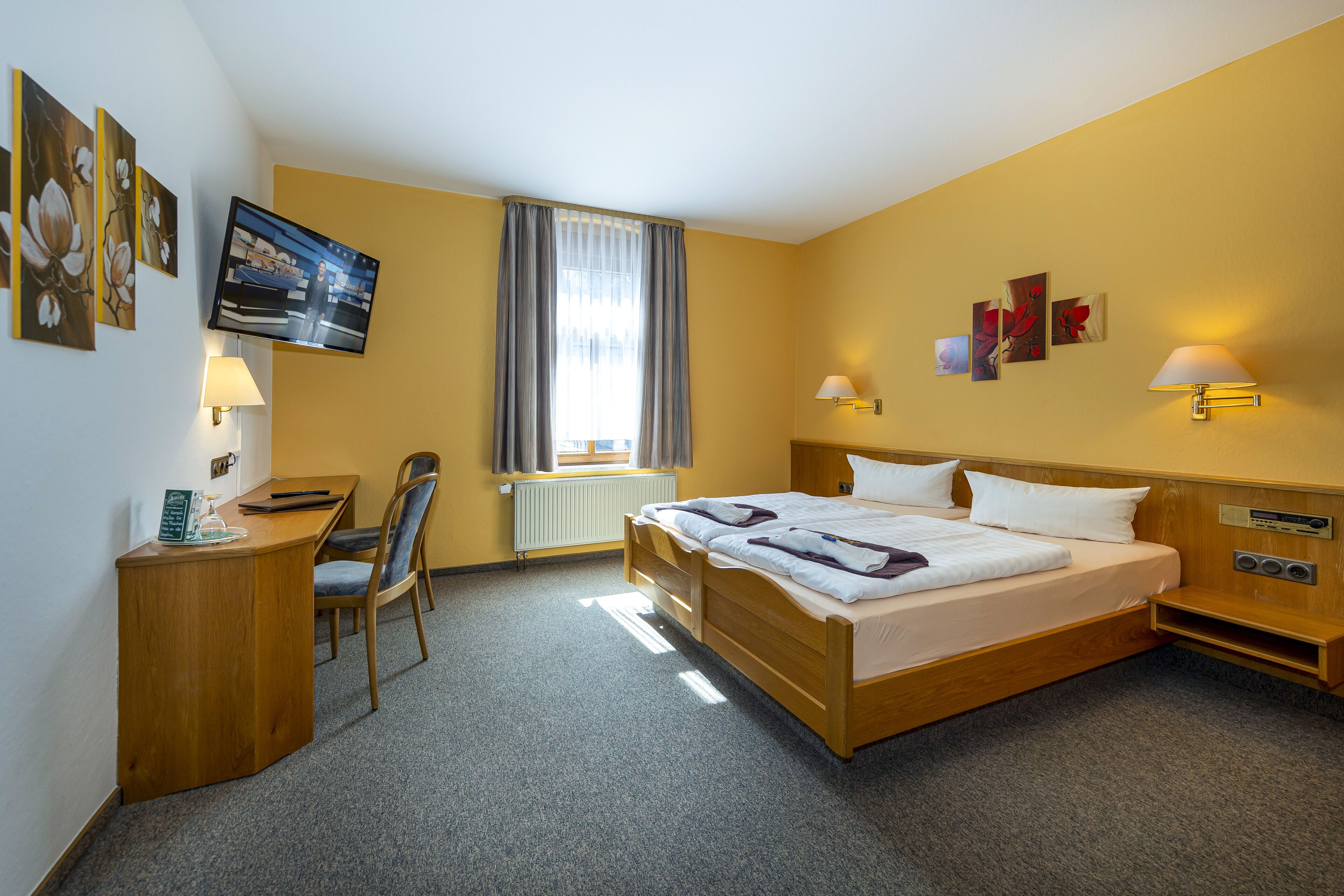 A hotel room with a bed, desk, chair, and artwork on the walls.