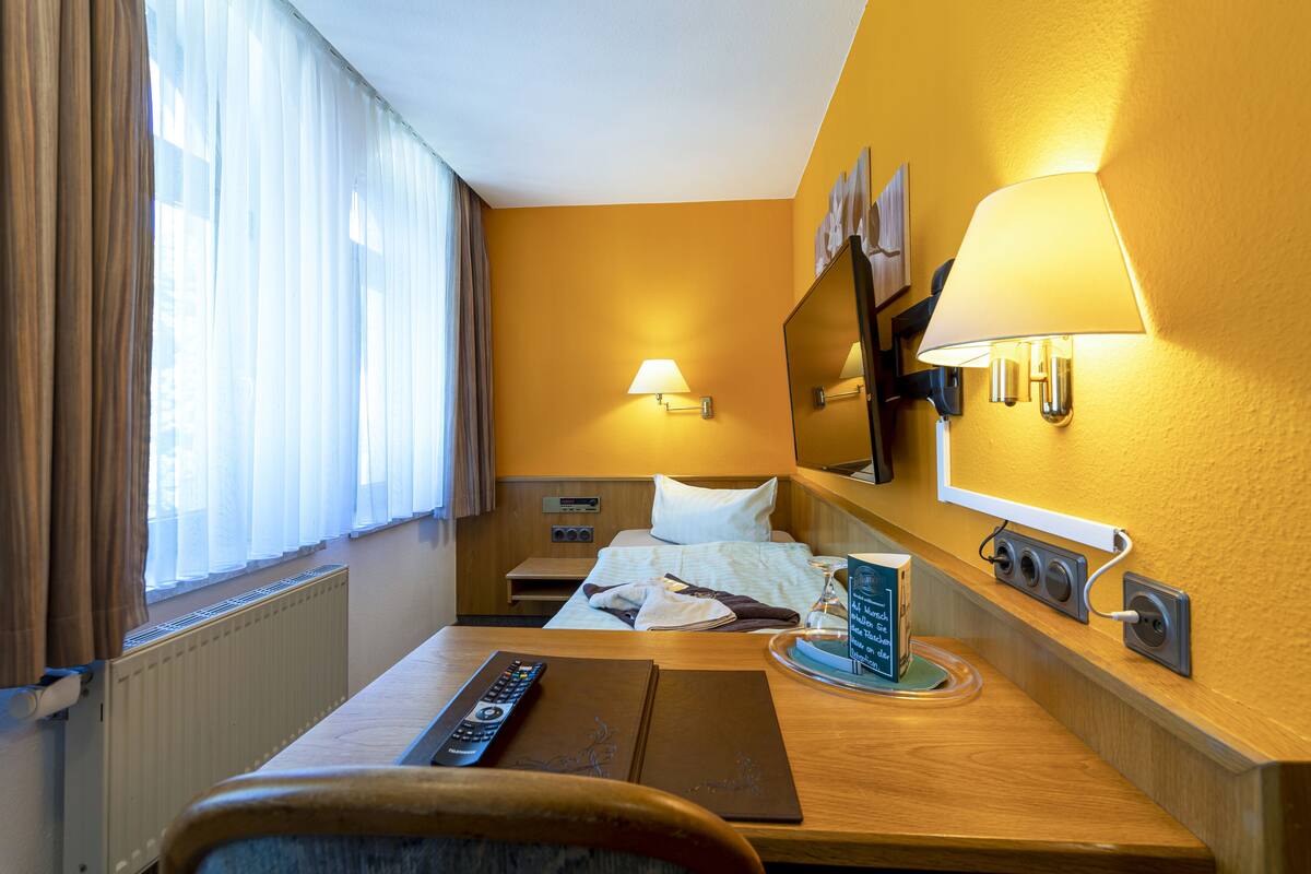 A hotel room with a bed, a desk with a remote control, a lamp, and a mirror.