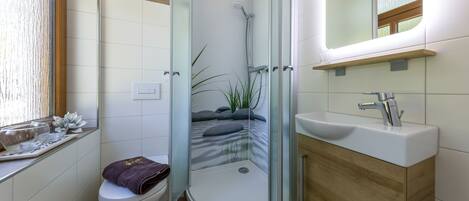 Un baño moderno con ducha de vidrio, inodoro, lavamanos y espejo.