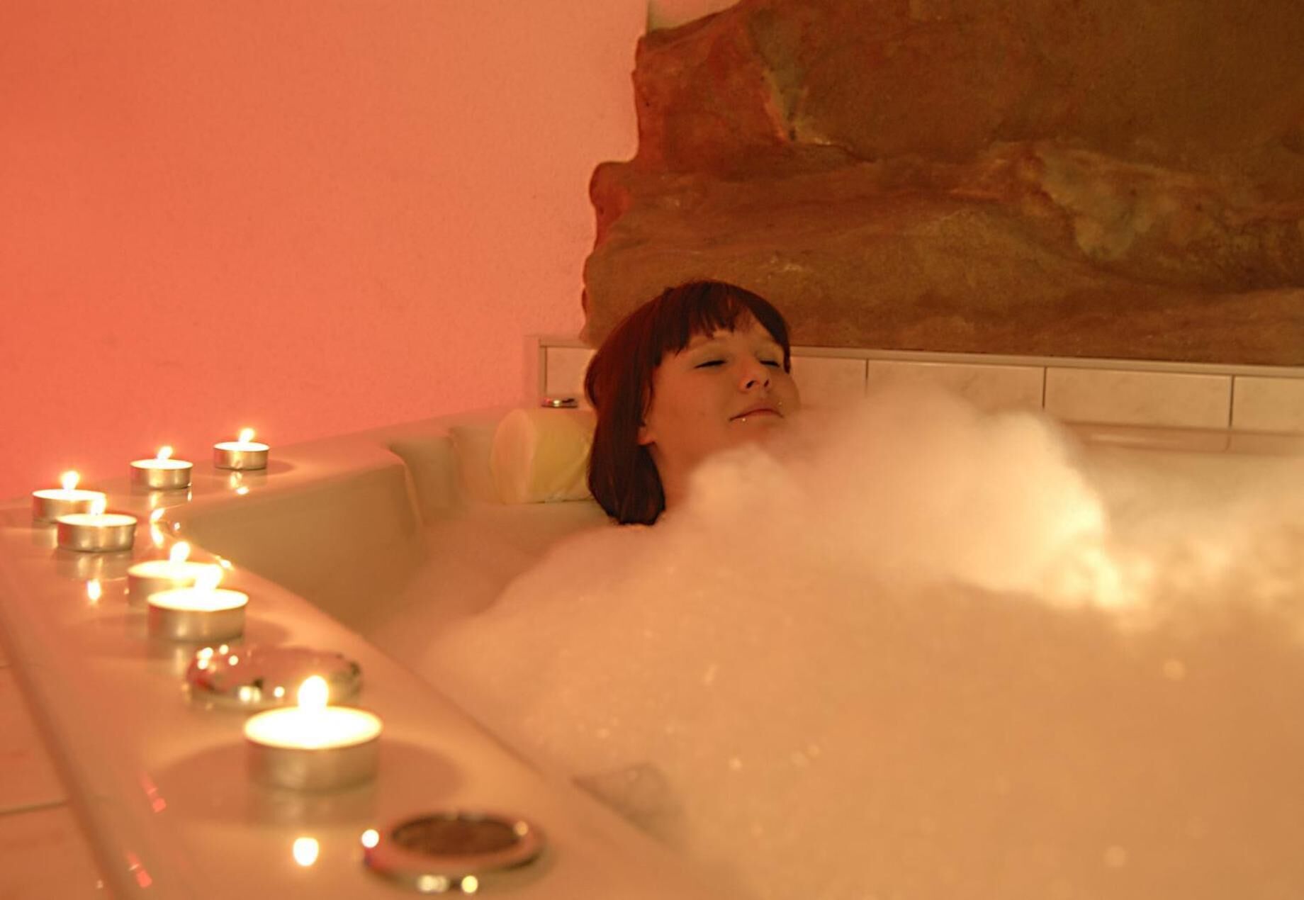 A person in a bathtub surrounded by candles.