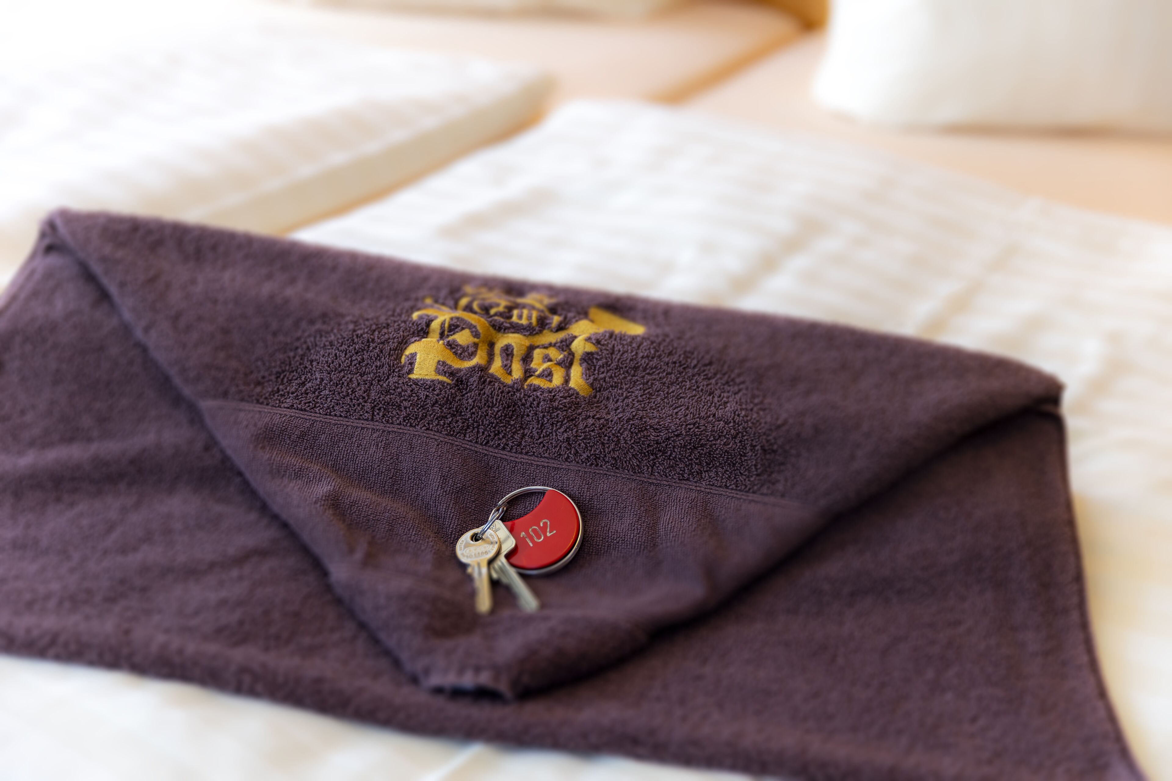 Una toalla morada con un logotipo y un llavero sobre una cama.