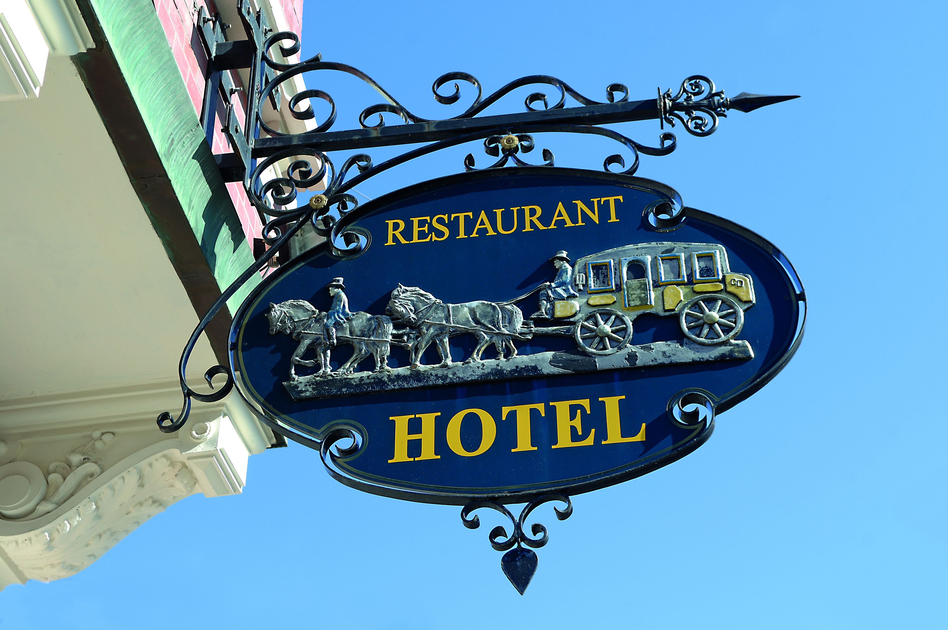 Señal de un restaurante y hotel con una ilustración de un carruaje tirado por caballos.