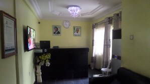 A reception area with a black reception desk, framed certificates on the wall, a clock, and a chandelier. - Terris Hotel and Suites (Lagos)