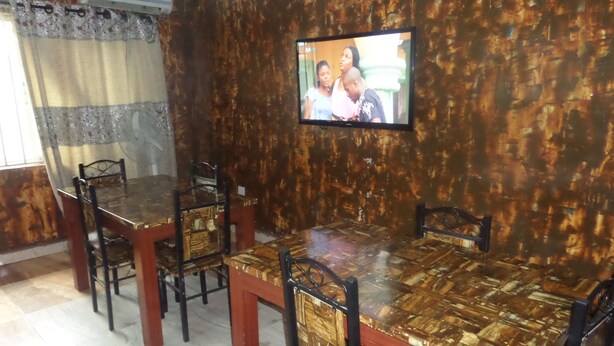 A dining area with a wooden table and chairs, a television mounted on the wall, and a window with curtains. - Terris Hotel and Suites (Lagos)