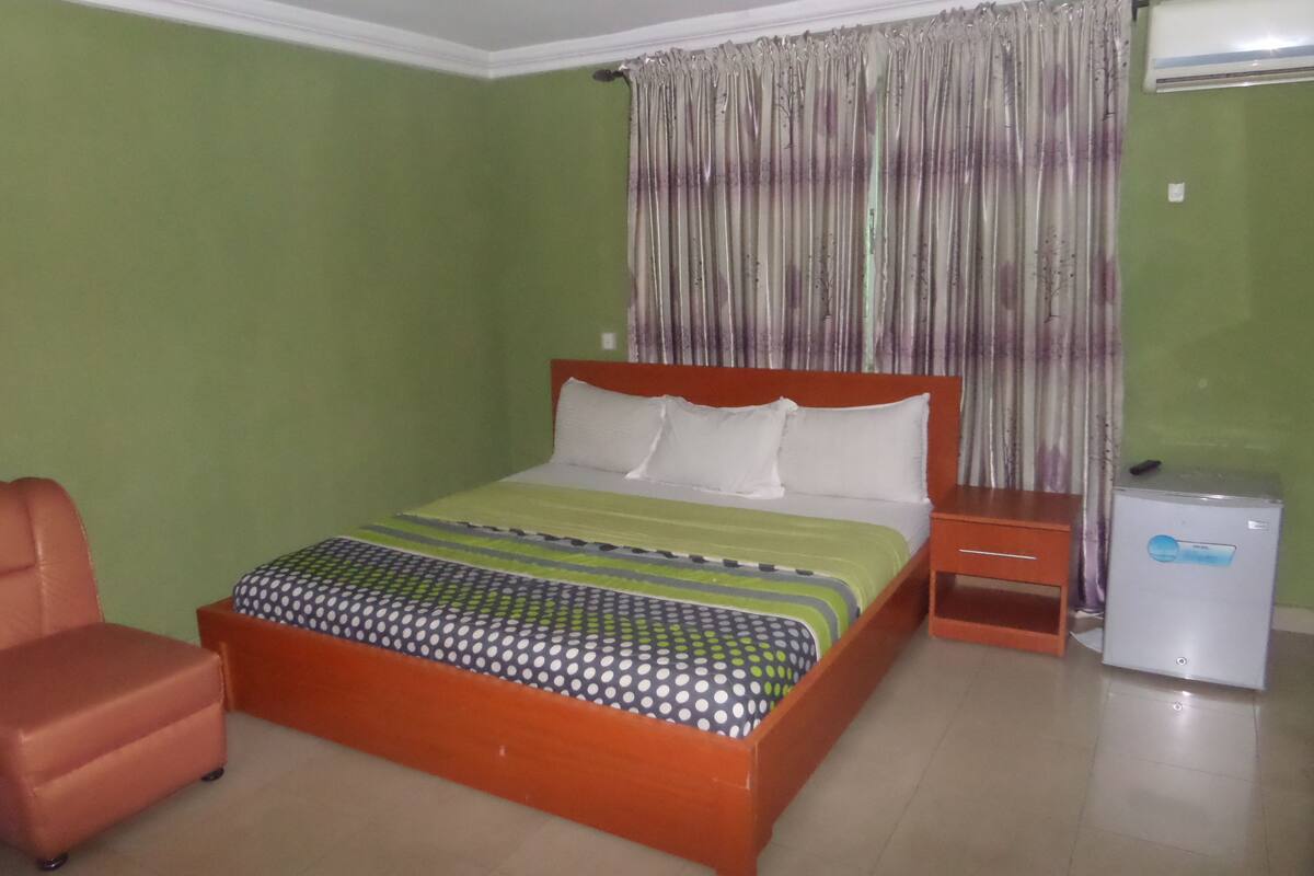 A bedroom with a bed, a nightstand, a chair, and an air conditioning unit.