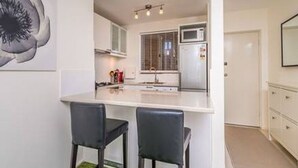 Eine moderne Küche mit weißer Arbeitsplatte, zwei Barhocker und einer Mikrowelle.
