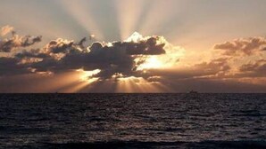 Ein Sonnenuntergang über dem Meer, wobei Sonnenstrahlen durch Wolken brechen.