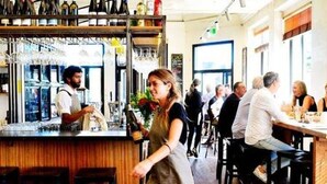 Eine Bar mit einem Barkeeper, Gästen an Tischen und einer Theke mit Flaschen und Gläsern.