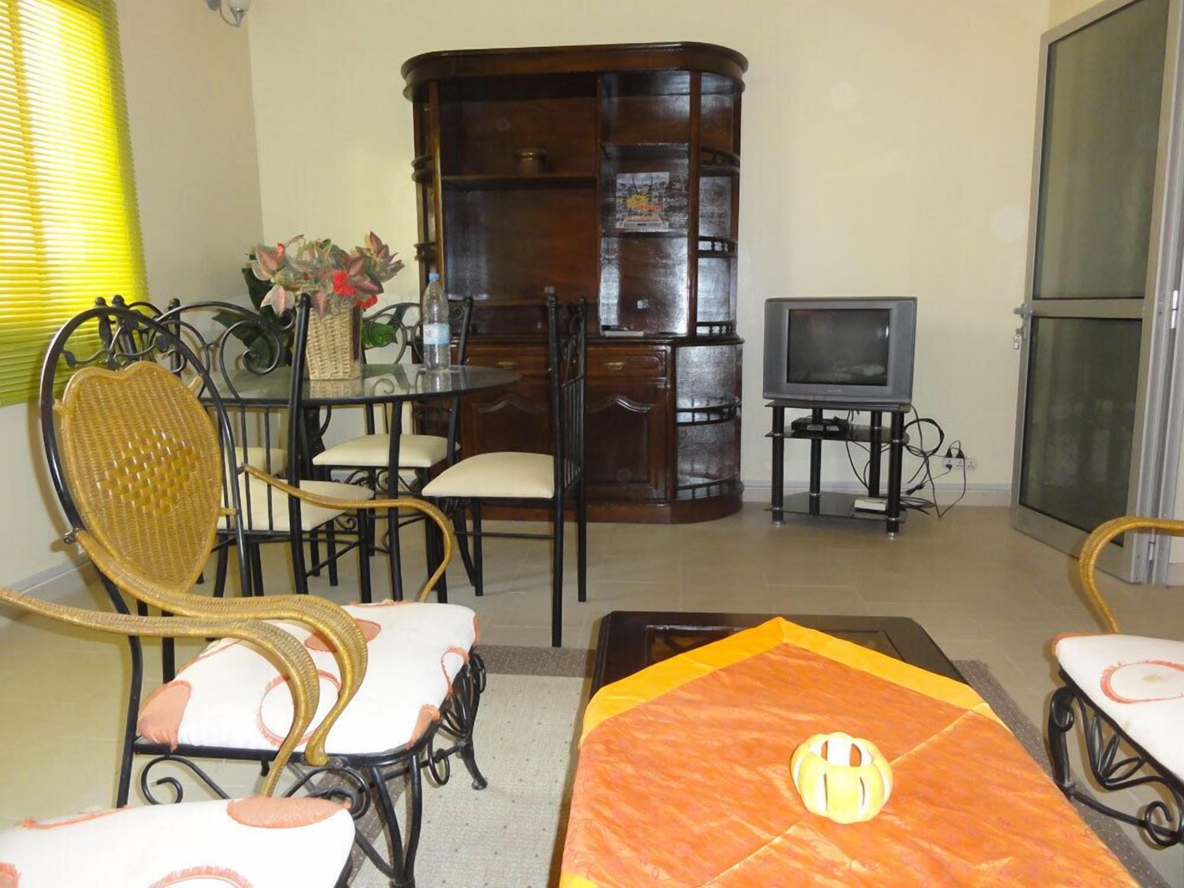 A living room with a wooden cabinet, a television, wicker chairs, and a patterned rug.