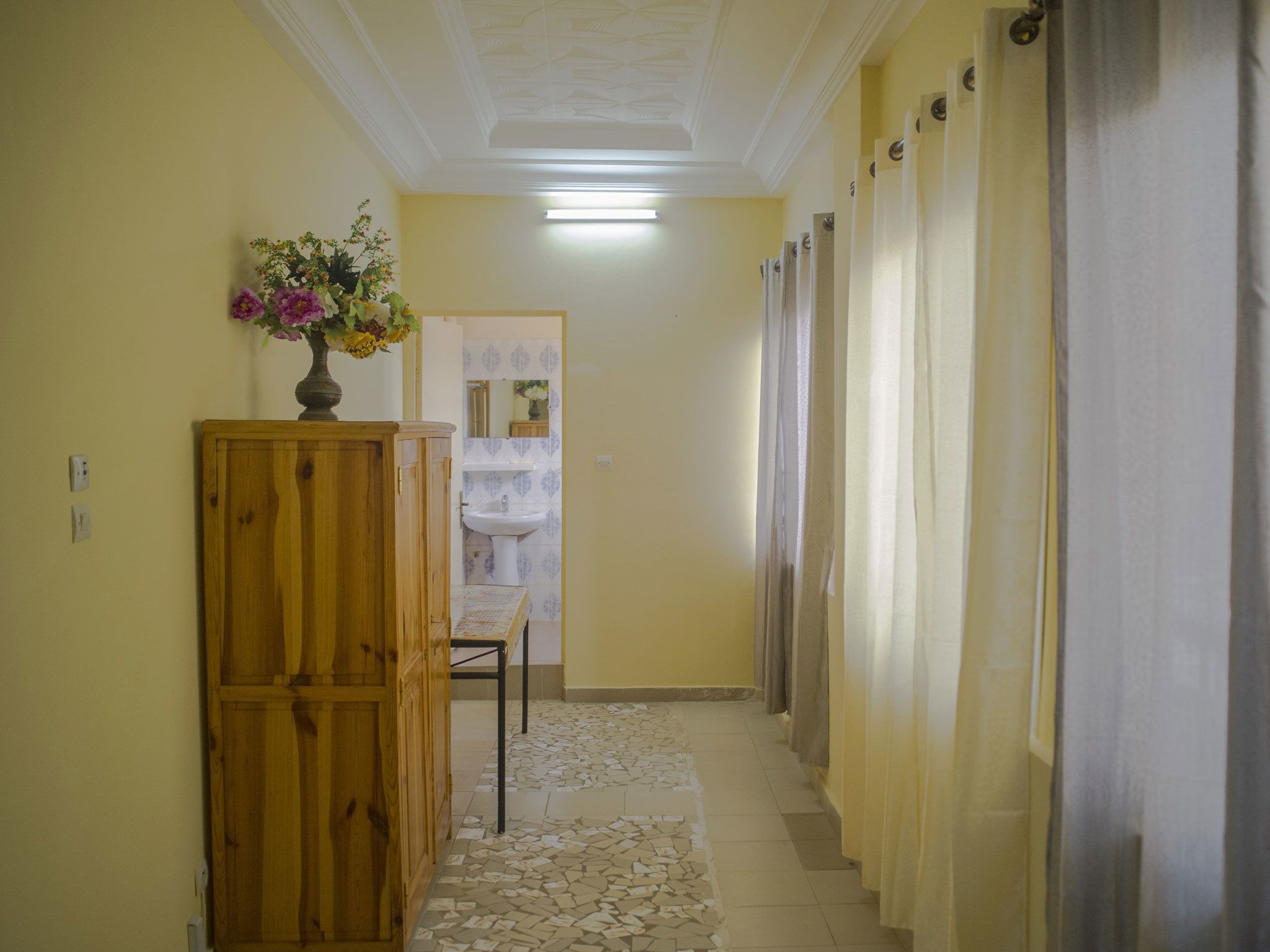 A narrow hallway with a wooden cabinet, a tiled floor, and a mirror on the wall.