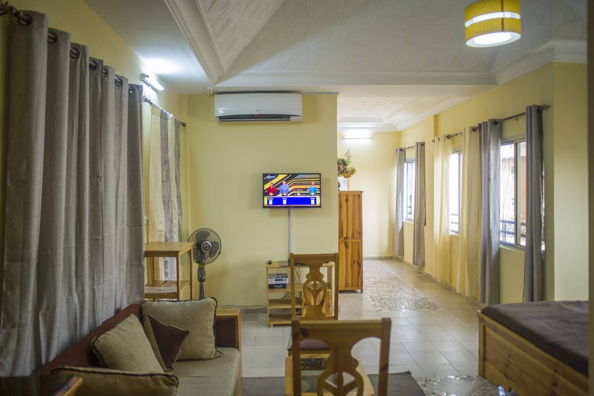 A living room with a sofa, a wooden chair, a TV, and a fan.
