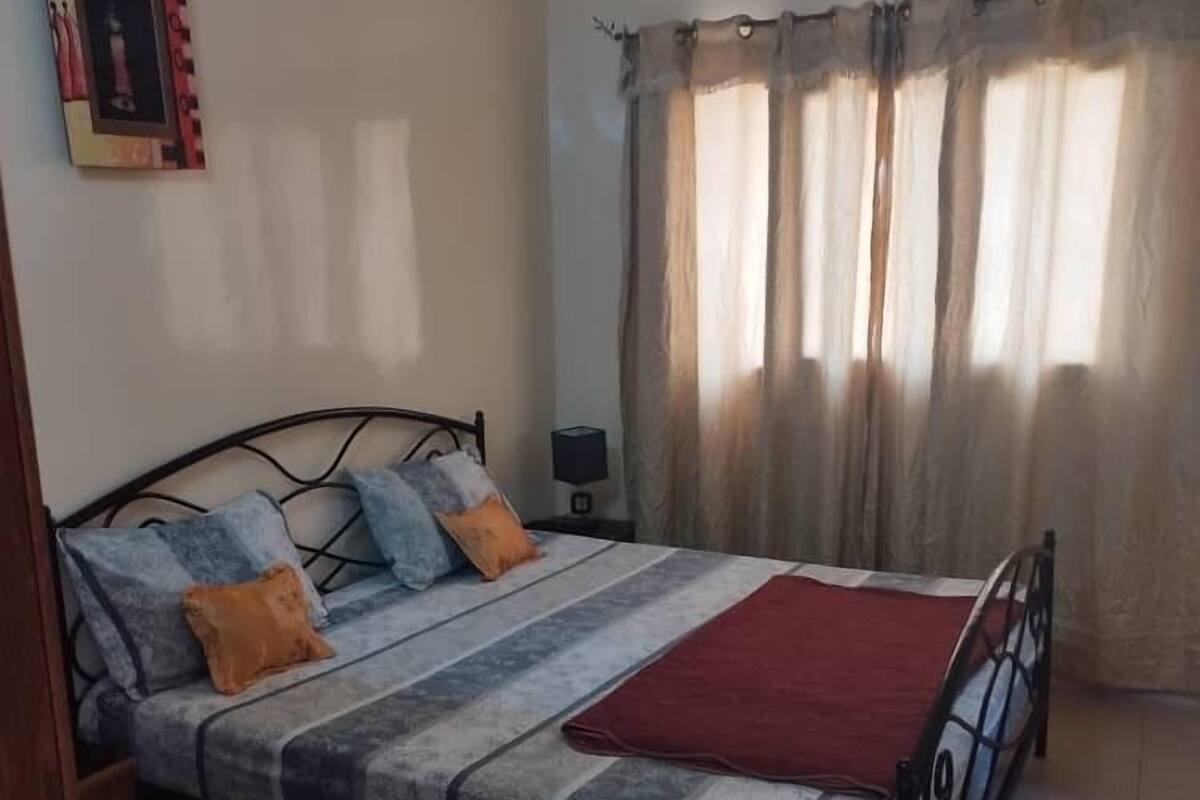 A bedroom with a bed, pillows, a nightstand, and a window with curtains.