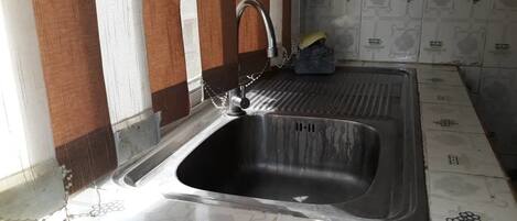 A kitchen with a stainless steel sink, a window with a brown frame, and patterned floor tiles.