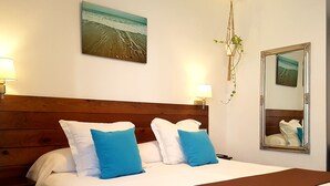 A hotel room with a wooden headboard, a large bed with white and blue pillows, a wall-mounted mirror, and a beach-themed painting. - Hostal Casa del Mar (Altea)