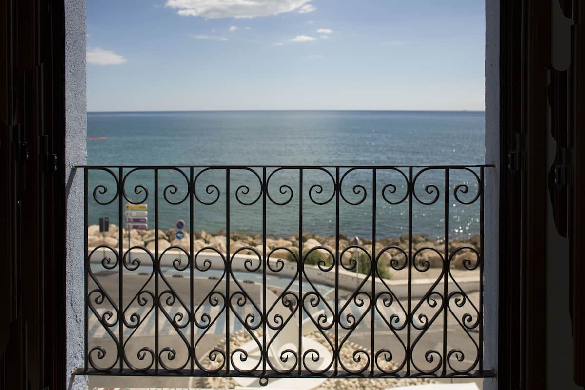 A view through a wrought iron gate with a clear sky and calm sea.