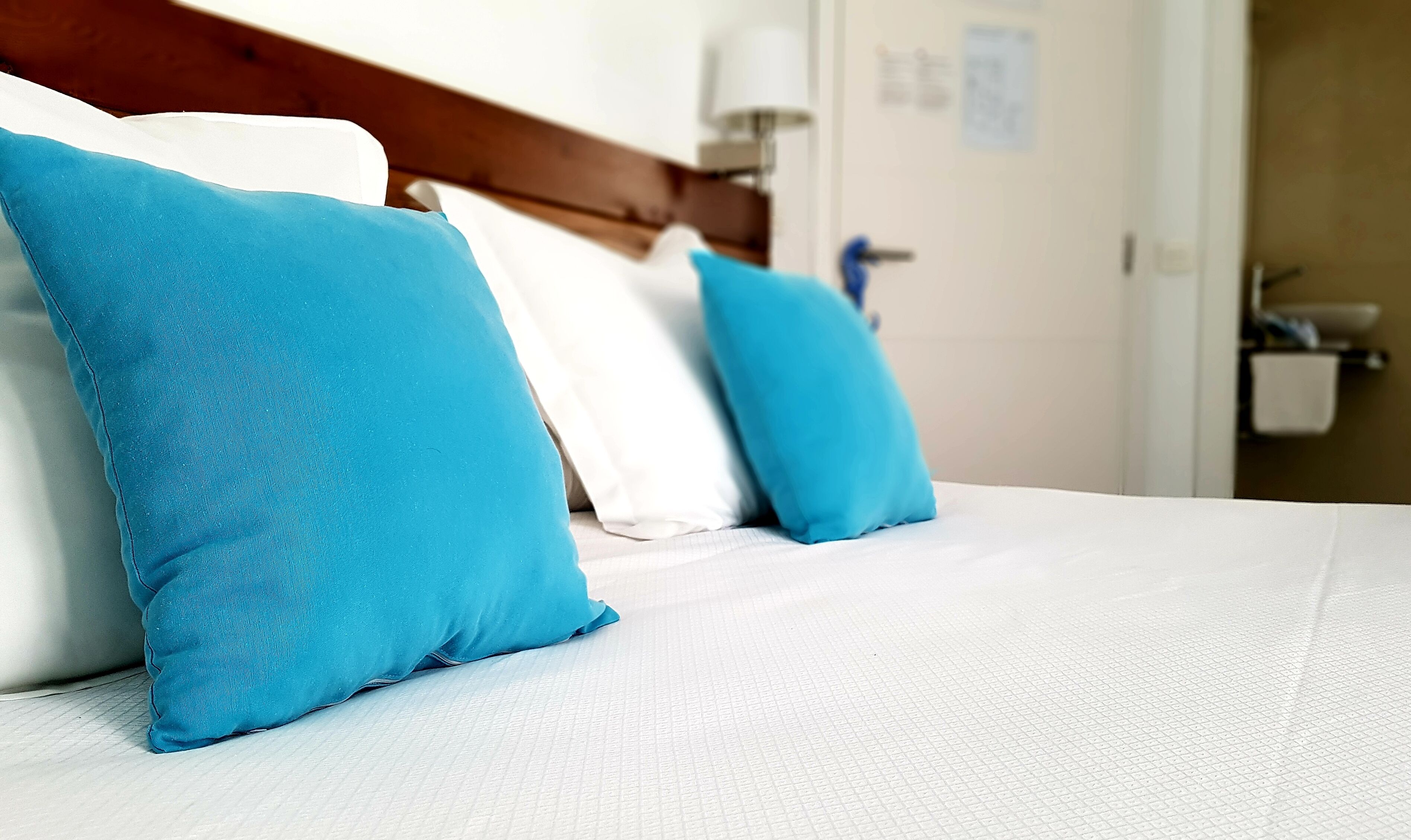 A neatly made bed with white bedding and two bright blue pillows.