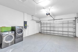 A clean, modern laundry room with industrial-style washers and dryers, a large garage door, and a ceiling-mounted projector.