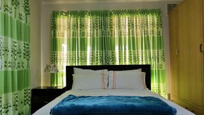 A neatly made bed with white and blue bedding, a wooden wardrobe, and green patterned curtains. - ParkViewAtMontagueFarm (Pooraka)