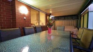 A glass-top dining table with chairs, a vase with flowers, and a brick wall. - ParkViewAtMontagueFarm (Pooraka)