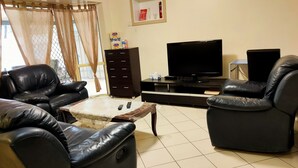 A living room with leather sofas, a TV, a cabinet, and a window with curtains. - ParkViewAtMontagueFarm (Pooraka)