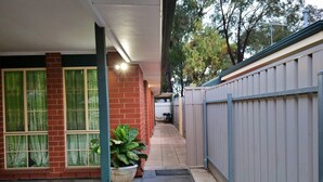 A narrow pathway leading to a building with a brick facade and large windows with green curtains. A potted plant is visible on the left side. - ParkViewAtMontagueFarm (Pooraka)