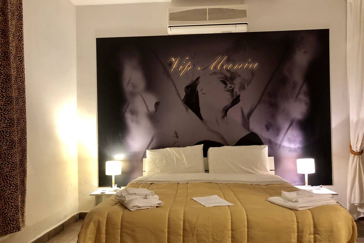 Habitació d'hotel amb un llit gran, almoines blanques, una colcha daurada i un mural a la paret.