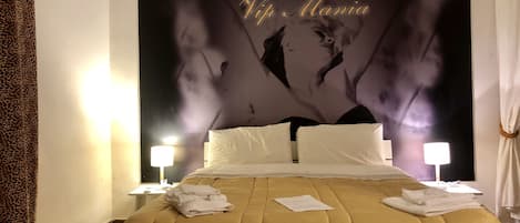 A hotel room with a large bed, white pillows, a gold-colored bedspread, and a wall mural.