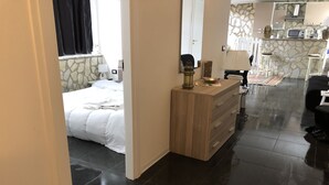 A hotel room with a bed, a wooden dresser, a small kitchen area with a microwave, and a stone wall. - Dolce Vita Casa Vacanze (Carini)