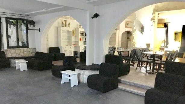 A spacious living area with a stone accent wall, black sofas, white tables, and a dining area with a table and chairs. - Dolce Vita Casa Vacanze (Carini)