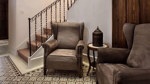 Una escalera con barandilla de hierro forjado, suelo estampado y dos sillones de cuero.