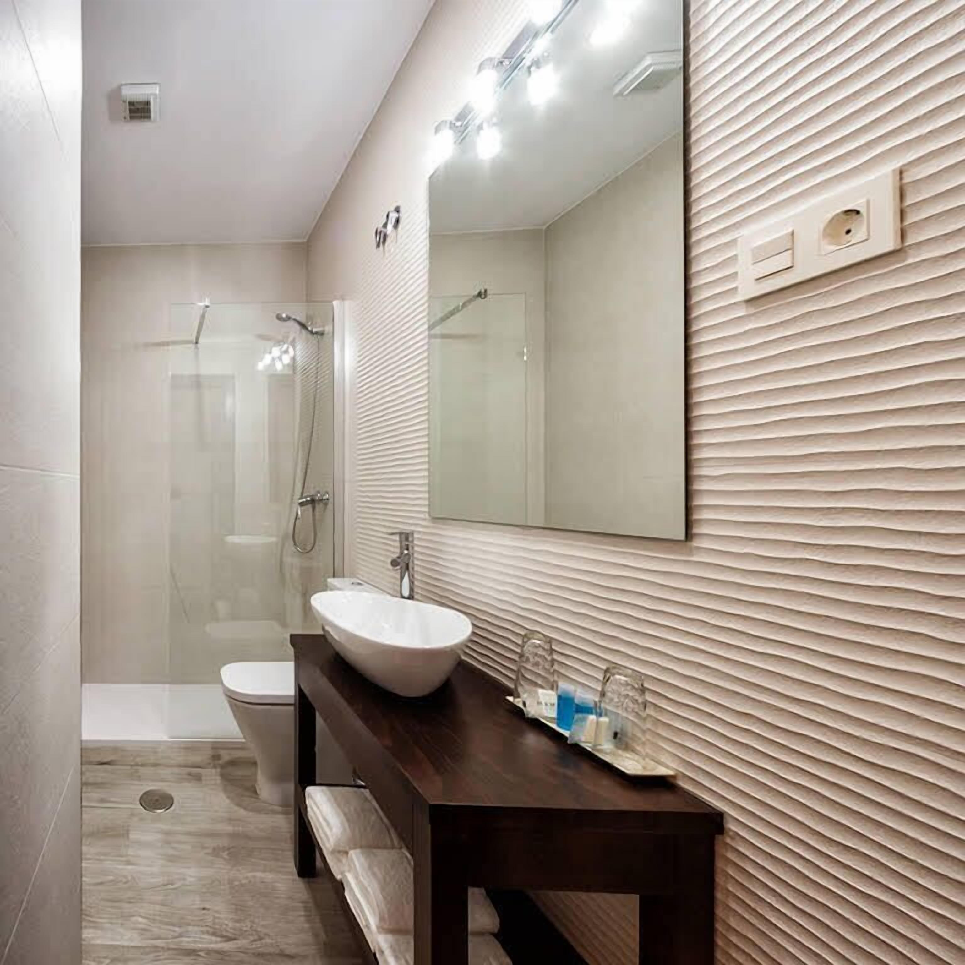 Un baño moderno con ducha envuelta en vidrio, un lavabo blanco y un mueble de tocador de madera.