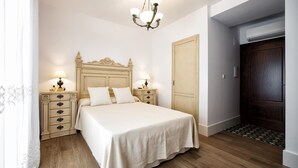 Un dormitorio con una cama grande, dos mesitas de noche con lámparas, suelo de madera y una puerta de madera oscura.